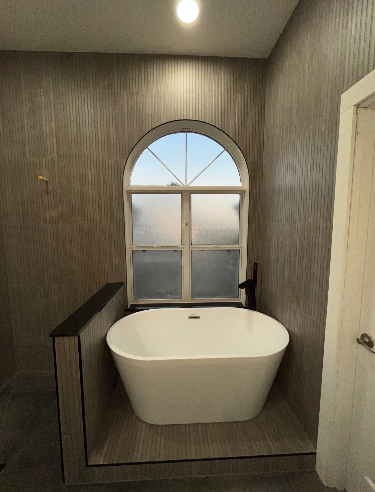Bathroom remodel detail showing tiled walls and arched window